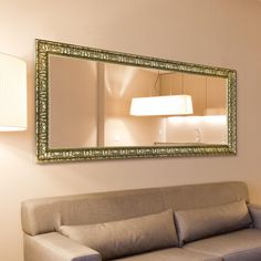 a couch sitting under a large mirror next to a wall mounted lamp and lampshade