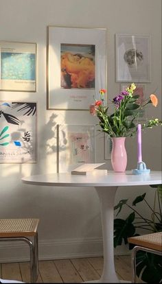 a white table topped with a vase filled with flowers next to pictures on the wall