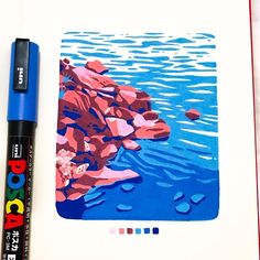 a blue marker is next to a drawing book with watercolors on it and an image of rocks in the water