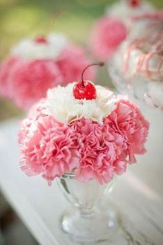 a vase filled with pink carnations and a cherry sitting on top of it