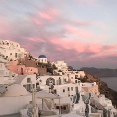 the sky is pink and purple as it sets on top of a hill with white buildings
