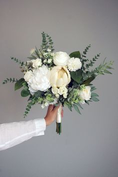 a bouquet of white flowers being held by a person's hand against a gray wall