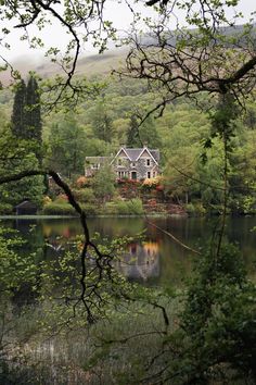 a large house sitting on top of a lush green hillside next to a lake surrounded by trees