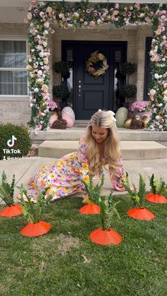 a woman laying on the ground in front of a house with fake flowers around her
