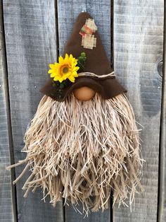 a scarecrow with a hat and sunflower on it's head hanging from a wooden fence