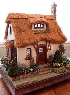 a small house with a thatched roof and flowers on the ground next to a window