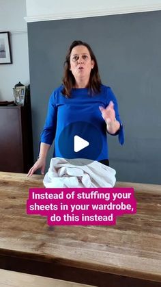 a woman standing in front of a wooden table with white sheets on it and the words instead of stuffing your sheets in your wardrobe, do this instead