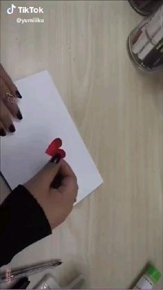 someone is writing on a piece of paper with a heart drawn on it and holding a pen
