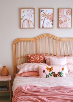 a bed with pink sheets, pillows and pictures on the wall above it's headboard