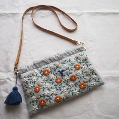 an embroidered purse with tassels and flowers on the front is laying on a white sheet