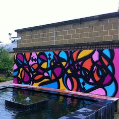 colorful graffiti on the side of a building next to a water feature in a garden