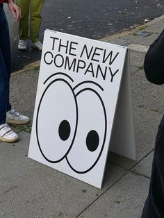 a sign that says the new company with two eyes on it and people standing around