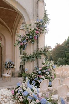 an outdoor ceremony with chairs, flowers and greenery on the side of the building