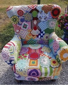 a colorful patchwork chair sitting on top of a gravel ground next to flowers and potted plants