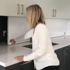 a woman standing in front of a white counter top next to a sink and oven