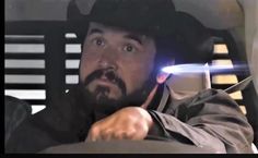 a man wearing a hat and holding a light saber in his hand while sitting in a car