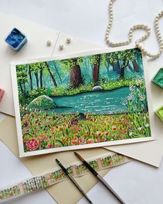a card with a painting of a pond surrounded by flowers and other crafting supplies
