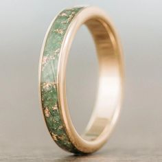 a gold ring with green marble inlays on the outside and inside, sitting on a wooden surface