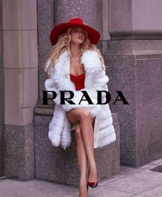 a woman in a red hat and white fur coat sitting on a ledge with her legs crossed