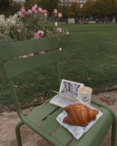 a croissant, coffee cup and newspaper on a green bench