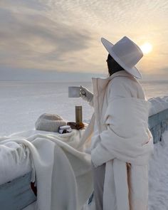 a woman in white is standing by the water with a blanket and hat on her head