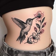 a woman's stomach with a hummingbird and flowers tattoo on her side belly