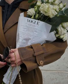 a woman in a trench coat holding flowers