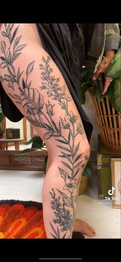 a woman's leg with tattoos on it and flowers in the background, next to a potted plant