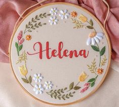 the embroidery is on top of a pink cloth with flowers and leaves around it that says, helema