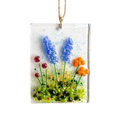 a glass ornament with flowers and berries hanging from a string on a white background