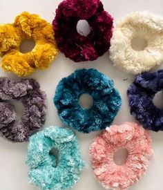six scrunffle hair ties in various colors on a white surface with one being pulled up to the side