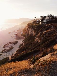 the sun is shining on an ocean side beach with houses and cliffs in the background