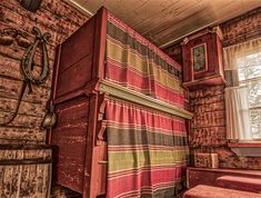 an old fashioned bedroom with red and yellow striped bedspread next to a window