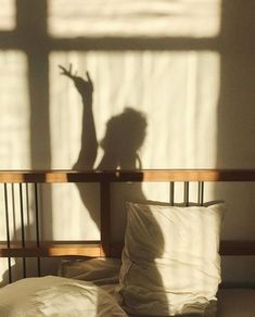 the shadow of a person standing on a bed in front of a window with white sheets