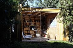 a shed with a chair and bookshelf in the back yard, surrounded by trees