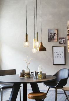 a dining room table with chairs and pictures on the wall above it, along with hanging lights