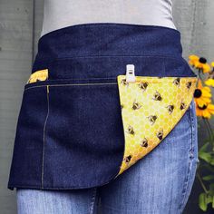 a woman is wearing a denim apron with bees on it and has her pocket open