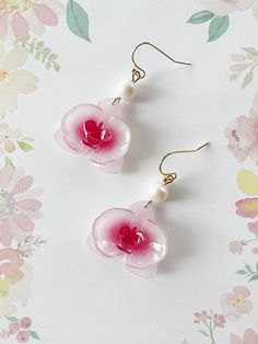 two pink flowers with pearls hanging from them on a white surface next to floral wallpaper