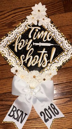 a decorated graduation cap with the words, one shot and two flowers on it sitting on top of a wooden table