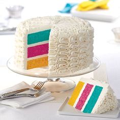 a white cake with multi - colored frosting sitting on top of a table next to silverware
