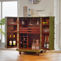 a wooden cabinet with wine glasses and bottles on wheels in front of a clock mounted to the wall