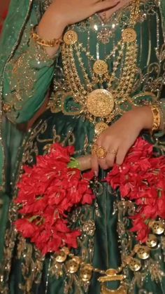a woman in a green dress with red flowers on her chest and gold jewelry around her neck