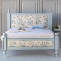 a white bed with blue flowers on the headboard and foot board in a bedroom