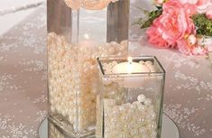 two square glass vases filled with pearls on top of a table next to pink flowers