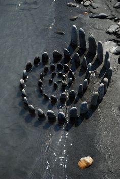 rocks are arranged in the shape of a spiral on the sand at the water's edge