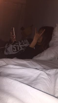 a woman laying in bed with her hand up to her face while holding a cell phone