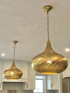 two golden lights hanging from the ceiling in a kitchen with granite counter tops and white cabinets