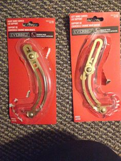 two pairs of gold colored metal hooks on carpeted floor next to each other in packaging