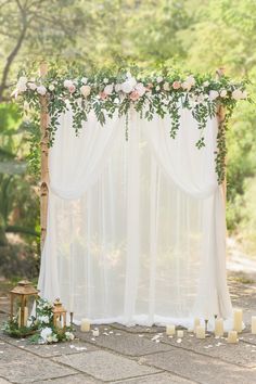 an outdoor wedding ceremony with white drapes and greenery on the side, candles in front of it