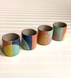three cups with different colors on them sitting next to each other in front of a white wall